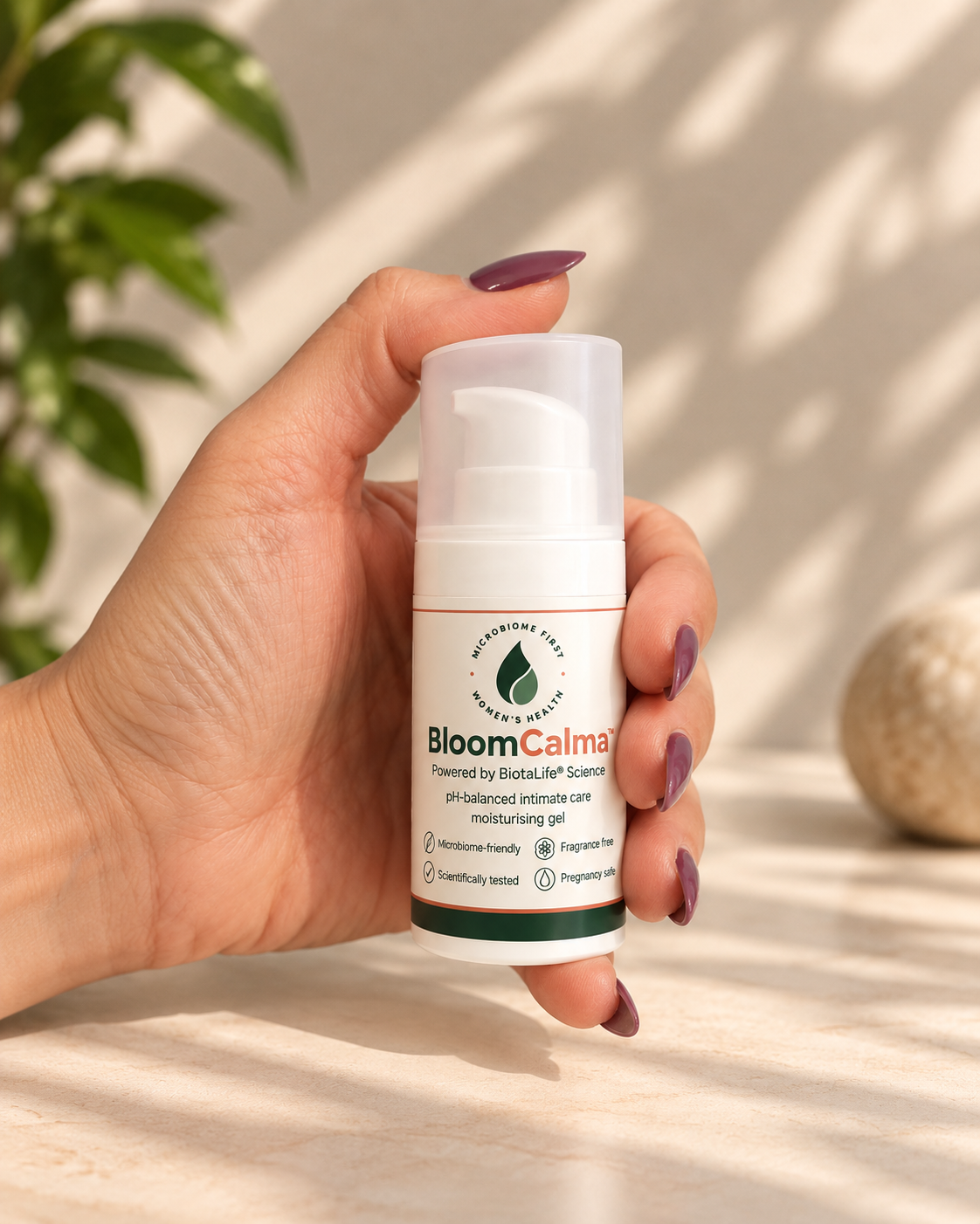Hand holding BloomCalma intimate moisturising gel in a 30ml airless pump bottle, against a warm cream background with soft botanical shadows and natural sunlight.